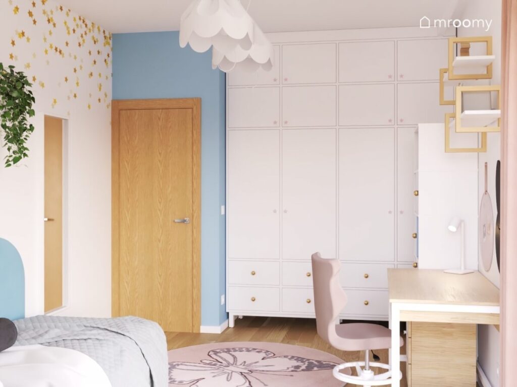Duża biała szafa ze złotymi gałkami dywan z motylem oraz lampy bezy w jasnym pokoju dziewczynki