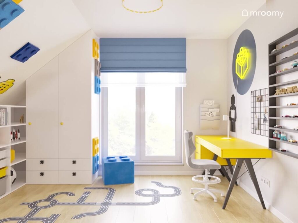 Jasny poddaszowy pokój dla chłopca z białą szafą żółtym biurkiem oraz dodatkami Lego i naklejką podłogową w kształcie jezdni