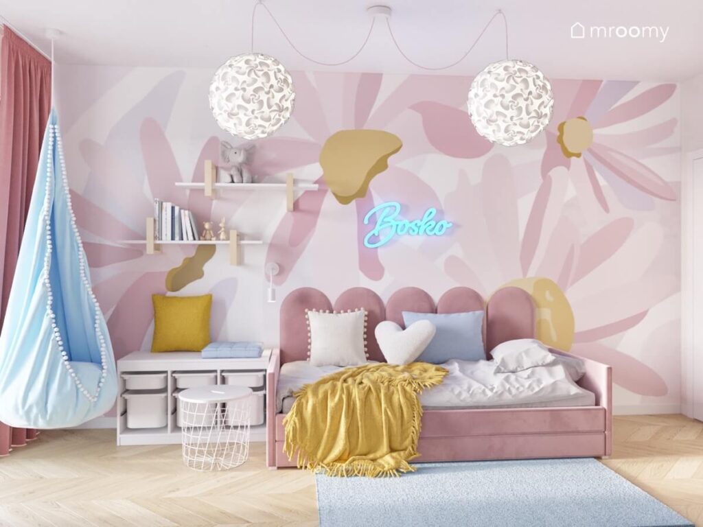 Strefa spania w pokoju dziewczynki z różowym tapicerowanym łóżkiem uzupełnionym miękkimi panelami oraz tapetą w kwiaty