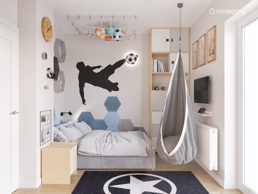 Łóżko w pokoju dla chłopca nad nim naklejka ścienna w kształcie piłkarza oraz lampka w kształcie piłki a obok fotel kokon