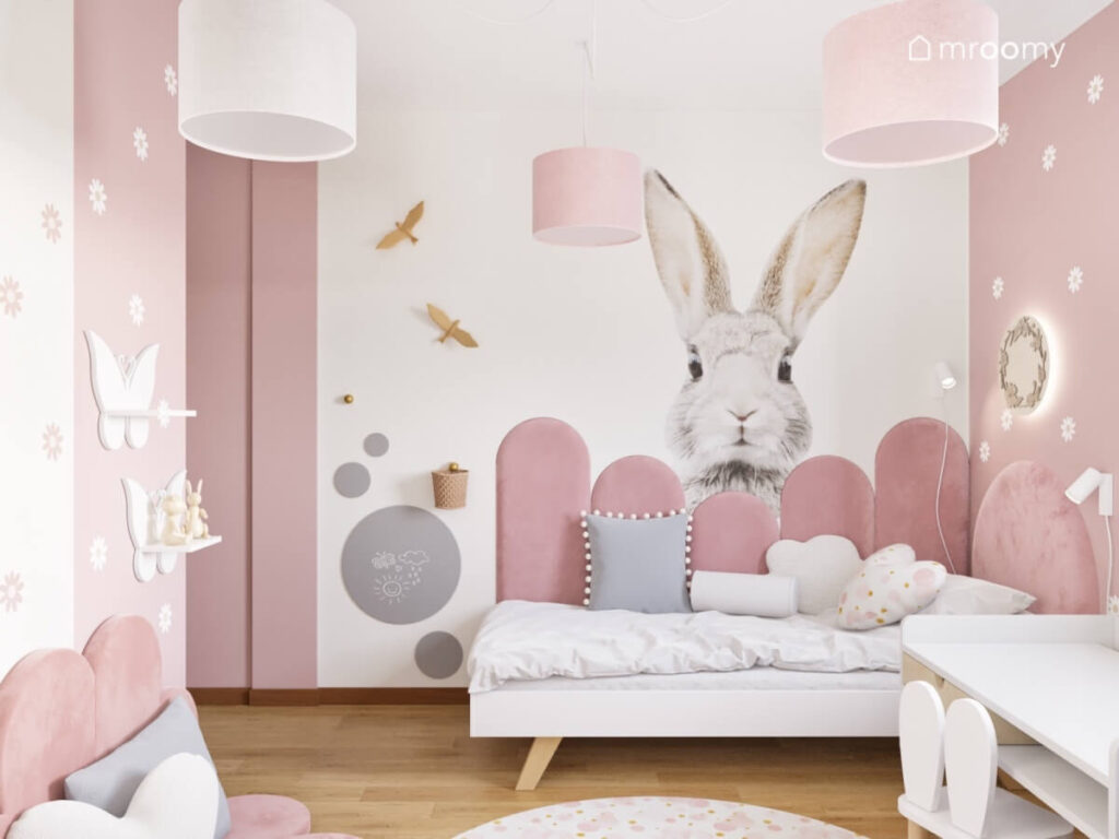 Strefa spania w biało różowym pokoju dla dziewczynki a w niej proste białe łóżko uzupełnione różowymi panelami oraz naklejką królik