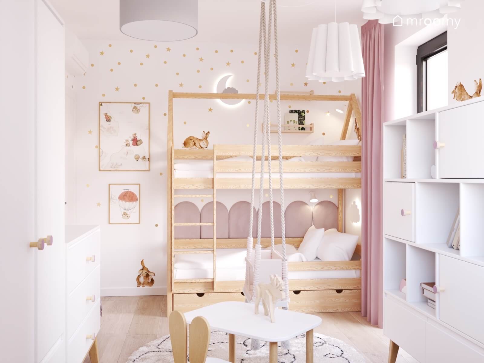 Drewniane łóżko piętrowe w pokoju dziewczynki a za nim ściana pokryta złotymi kropkami i gwiazdkami a na środku huśtawka